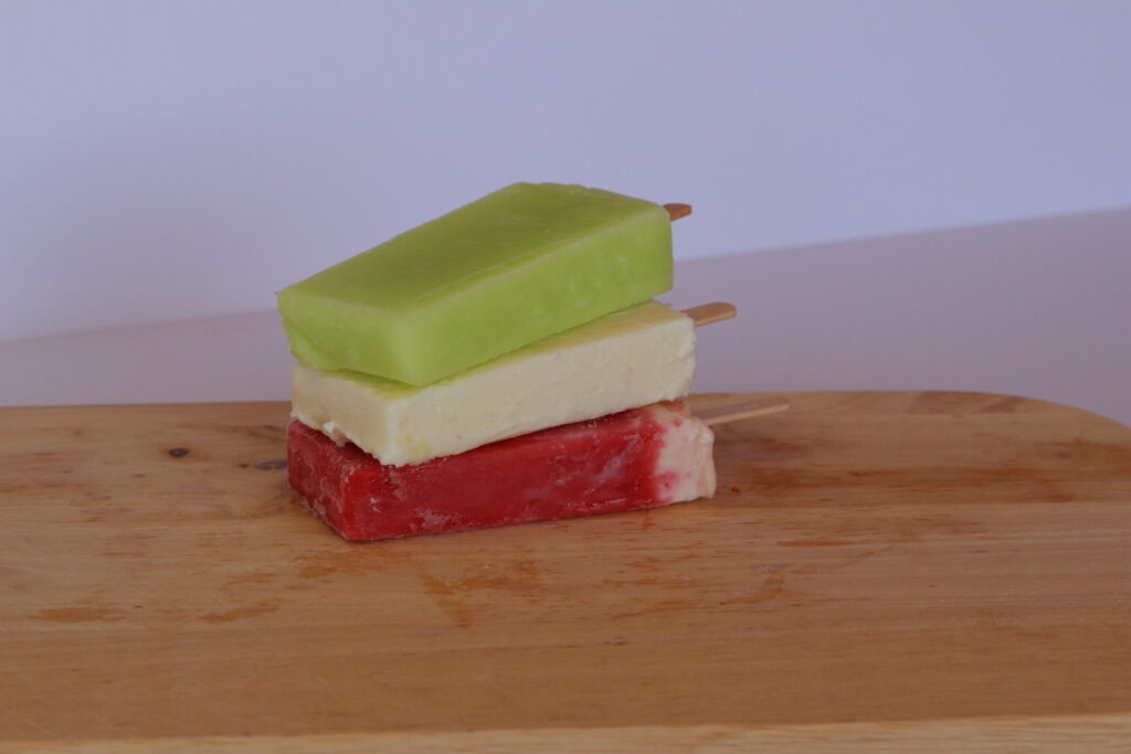 Lime, pineapple, and strawberry paletas stacked diagonally on wood board