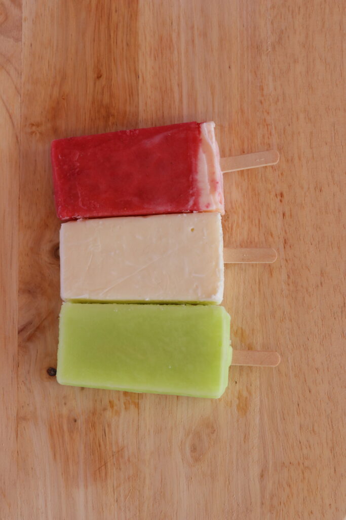 Lime, pineapple, and strawberry paletas layed out flat on a wood board