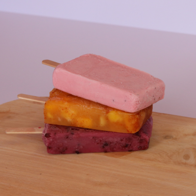 Trio of paletas stacked—strawberry, mango with chili, and blackberry—on a wooden board
